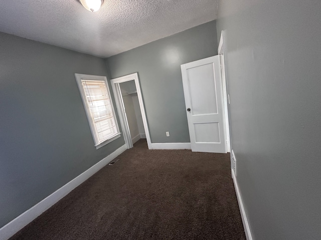 spare room featuring a textured ceiling, visible vents, baseboards, and dark colored carpet
