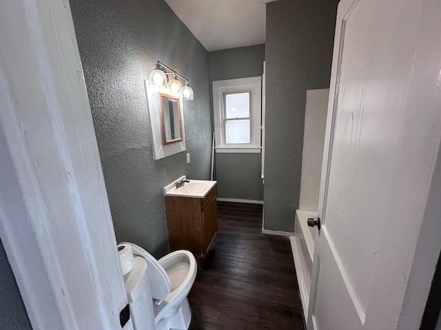 bathroom featuring wood-type flooring, a textured wall, baseboards, and vanity