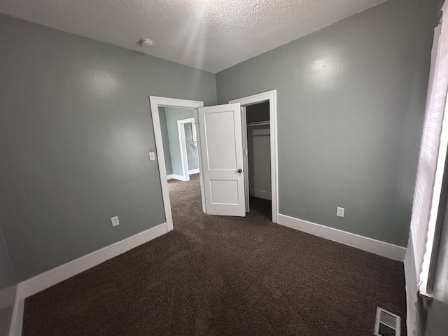 unfurnished bedroom featuring a textured ceiling, dark carpet, baseboards, visible vents, and a closet