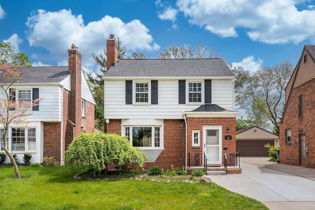 view of front facade with brick siding, a detached garage, an outbuilding, and a front yard