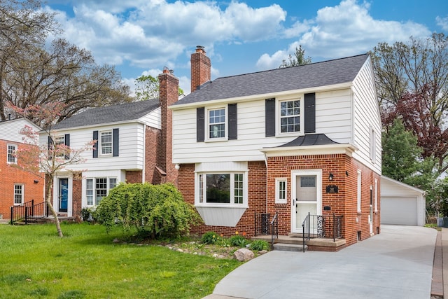 view of front of home with a shingled roof, a front lawn, brick siding, and an outbuilding
