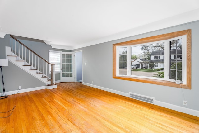 unfurnished living room featuring wood finished floors, visible vents, baseboards, and stairs