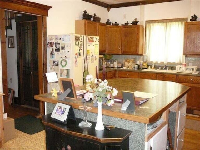 kitchen featuring brown cabinetry, a center island, wood finished floors, a sink, and freestanding refrigerator