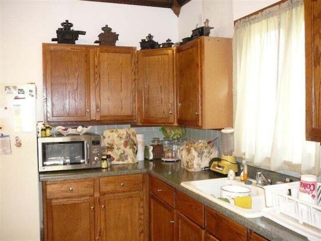 kitchen featuring a sink, brown cabinetry, freestanding refrigerator, stainless steel microwave, and tasteful backsplash