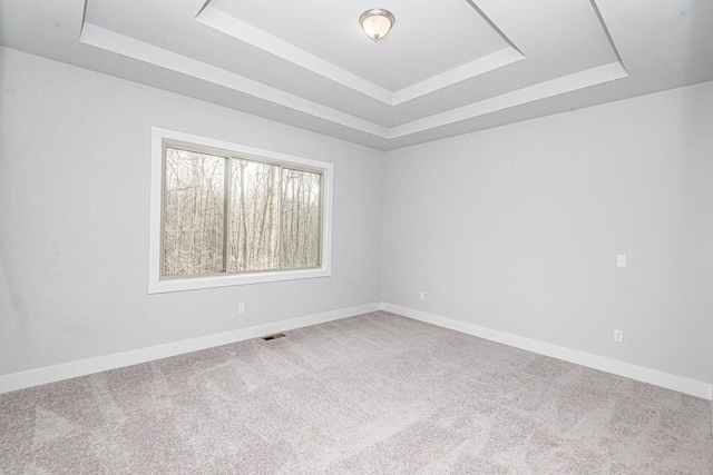 carpeted spare room with visible vents, a raised ceiling, and baseboards