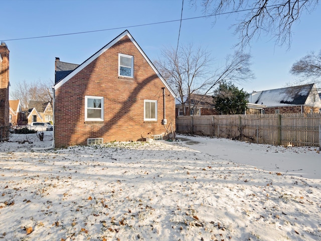 snow covered rear of property with fence, a chimney, and brick siding
