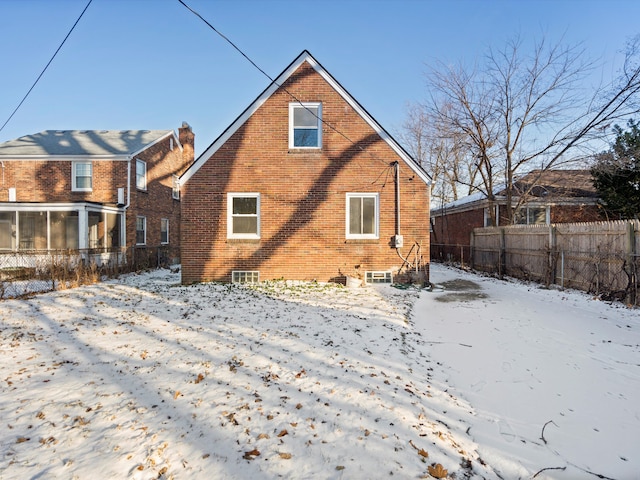 snow covered house with brick siding, fence, and a sunroom