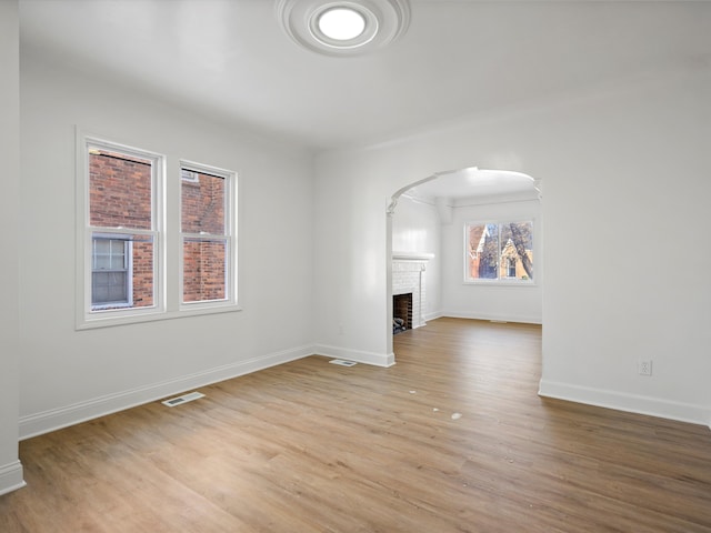 unfurnished living room featuring visible vents, arched walkways, a brick fireplace, baseboards, and light wood-style flooring