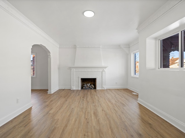 unfurnished living room with ornamental molding, a fireplace, light wood-style floors, baseboards, and arched walkways