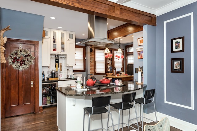 kitchen with beverage cooler, island range hood, dark wood-style floors, a kitchen bar, and backsplash