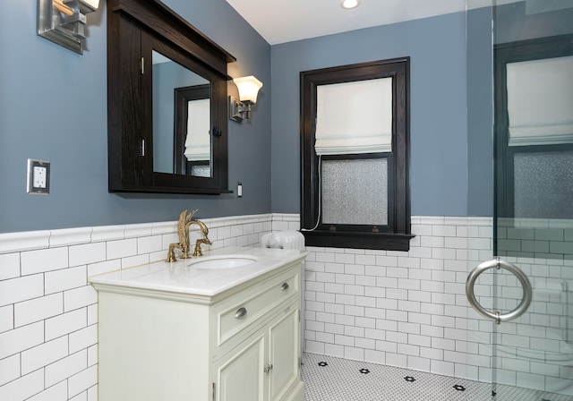full bath with vanity, tile walls, tiled shower, and a wainscoted wall