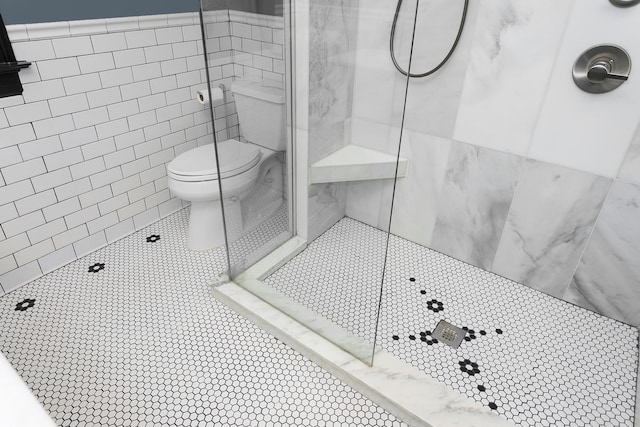 bathroom with tile patterned flooring, toilet, a wainscoted wall, tile walls, and tiled shower