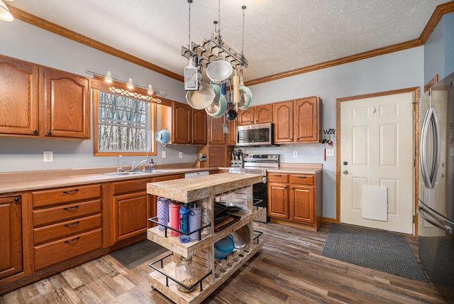 kitchen with brown cabinets, appliances with stainless steel finishes, a sink, light countertops, and wood finished floors