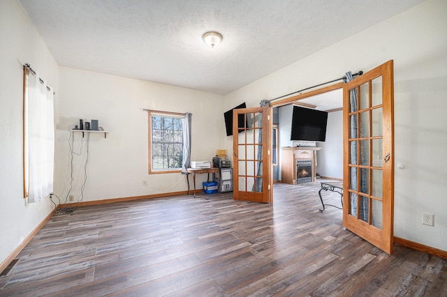 unfurnished room featuring wood finished floors, baseboards, a warm lit fireplace, a textured ceiling, and french doors