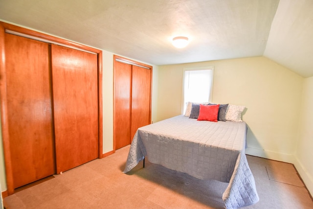bedroom featuring carpet floors, baseboards, multiple closets, and lofted ceiling