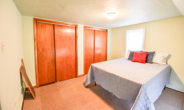 bedroom featuring two closets, baseboards, and light colored carpet