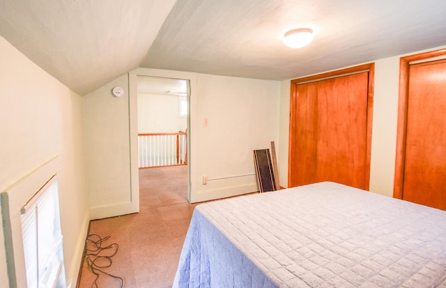 bedroom featuring baseboards, two closets, vaulted ceiling, and light carpet