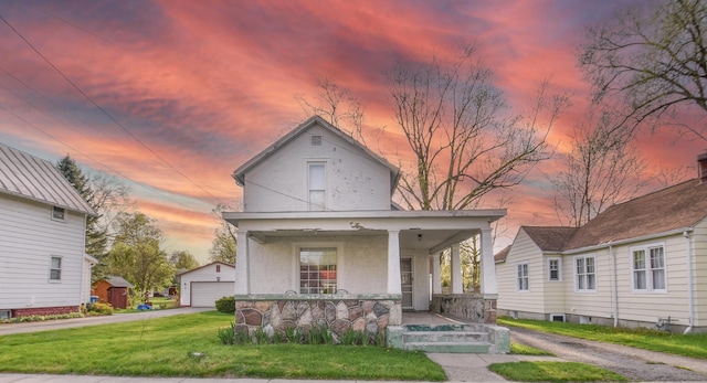 view of front of property with covered porch, an outbuilding, a detached garage, a front lawn, and stucco siding