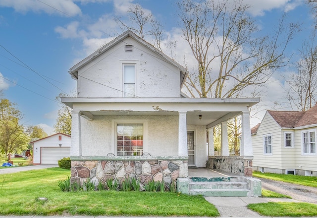 view of front facade featuring a detached garage, stucco siding, a porch, a front yard, and an outdoor structure