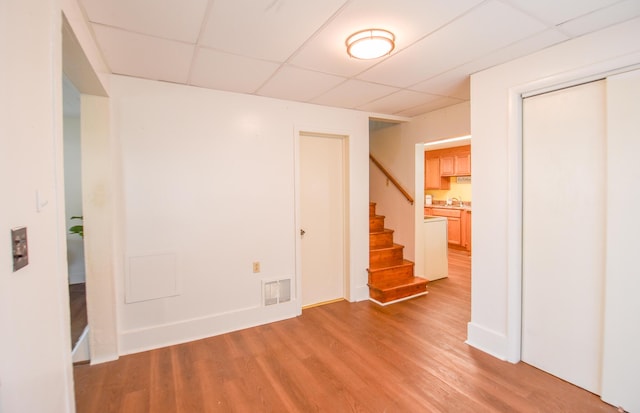 empty room featuring visible vents, a paneled ceiling, baseboards, light wood-style floors, and stairs
