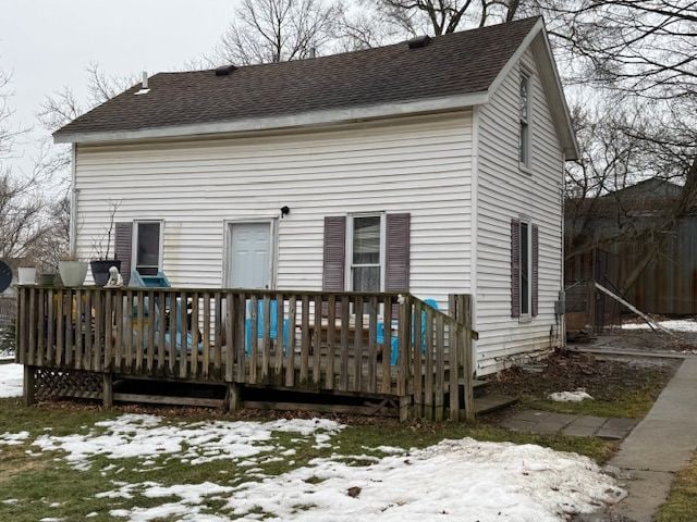 snow covered house with a shingled roof and a deck