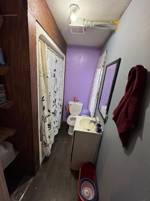 bathroom with vanity, toilet, wood finished floors, a shower with curtain, and visible vents