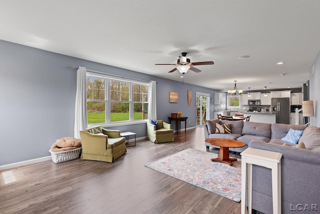 living area with recessed lighting, baseboards, wood finished floors, and ceiling fan with notable chandelier