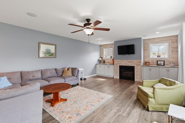 living area with ceiling fan, a glass covered fireplace, light wood-style flooring, recessed lighting, and baseboards