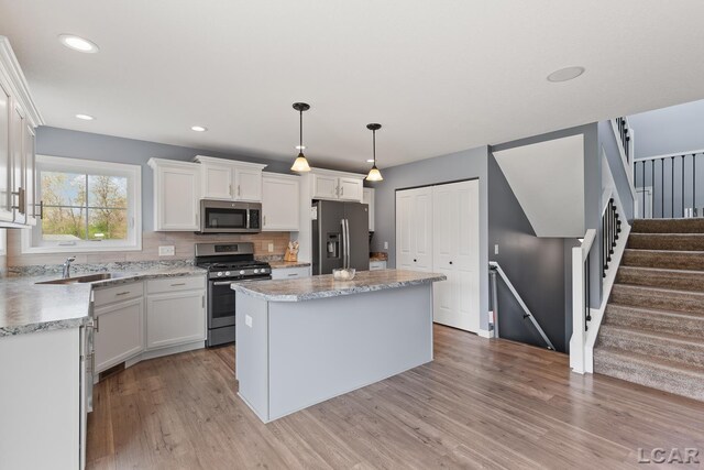 kitchen featuring a sink, light wood-style floors, stainless steel appliances, white cabinetry, and a kitchen island