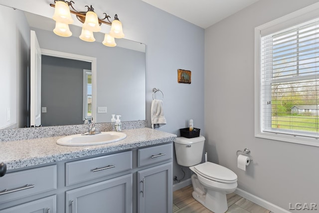 half bath featuring vanity, plenty of natural light, baseboards, and toilet