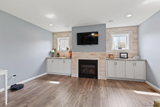 living area with a glass covered fireplace, baseboards, recessed lighting, and light wood finished floors