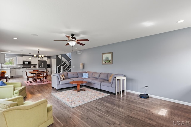 living area with dark wood-style flooring, ceiling fan with notable chandelier, baseboards, visible vents, and stairway