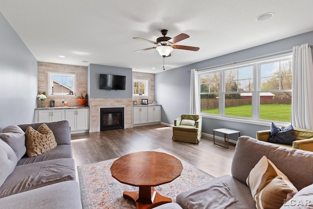 living area featuring plenty of natural light, a ceiling fan, a glass covered fireplace, and wood finished floors