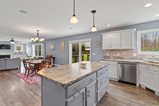 kitchen featuring a sink, a fireplace, backsplash, decorative light fixtures, and stainless steel dishwasher