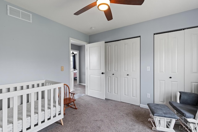 bedroom featuring a nursery area, ceiling fan, carpet floors, multiple closets, and visible vents