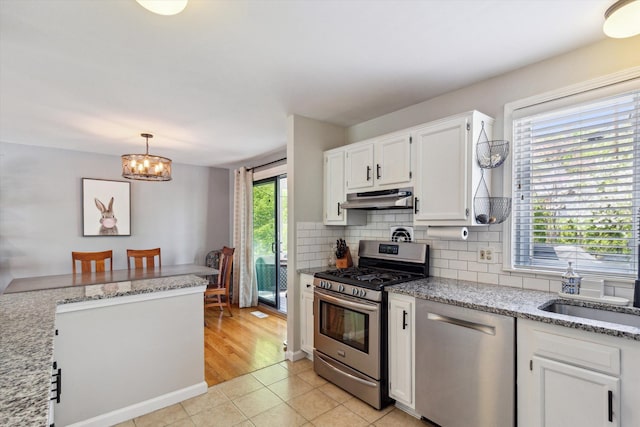 kitchen featuring stainless steel appliances, under cabinet range hood, backsplash, light tile patterned floors, and white cabinets