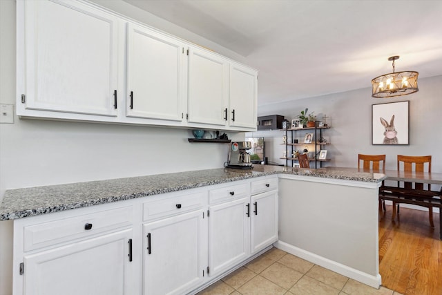kitchen with a peninsula, white cabinetry, light stone countertops, and a notable chandelier