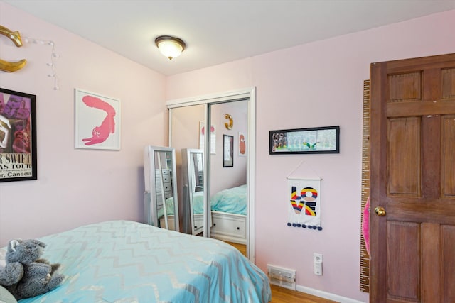bedroom with baseboards, a closet, visible vents, and wood finished floors