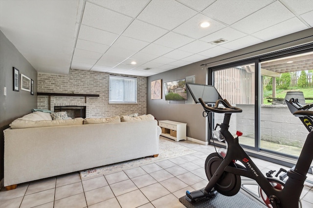 exercise area with brick wall, visible vents, a brick fireplace, light tile patterned floors, and a paneled ceiling