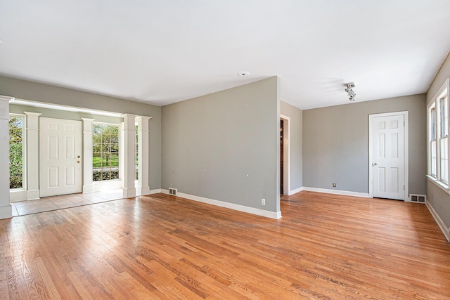 interior space featuring visible vents, light wood-style flooring, ornate columns, and baseboards