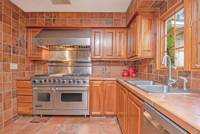 kitchen featuring decorative backsplash, tile countertops, a sink, ventilation hood, and stainless steel appliances