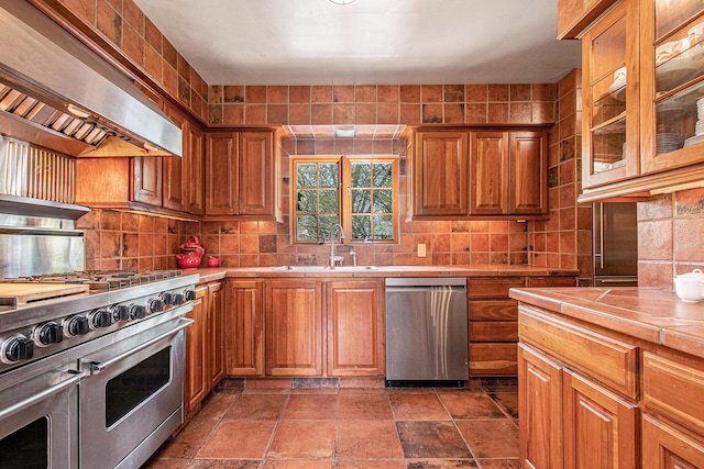 kitchen featuring tile countertops, tasteful backsplash, a sink, exhaust hood, and stainless steel appliances