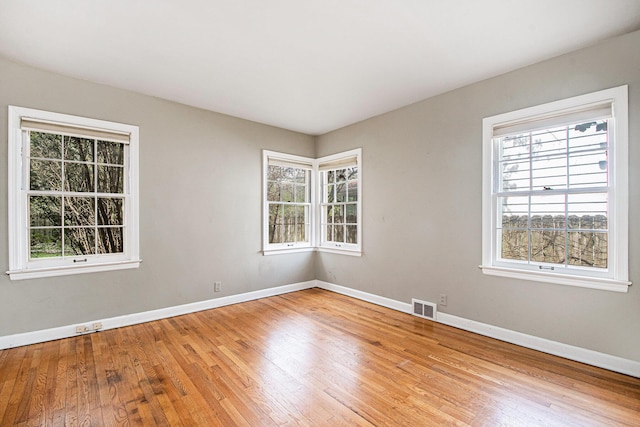 empty room with baseboards, visible vents, plenty of natural light, and light wood finished floors