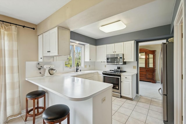 kitchen with light tile patterned flooring, appliances with stainless steel finishes, a breakfast bar, a sink, and a peninsula