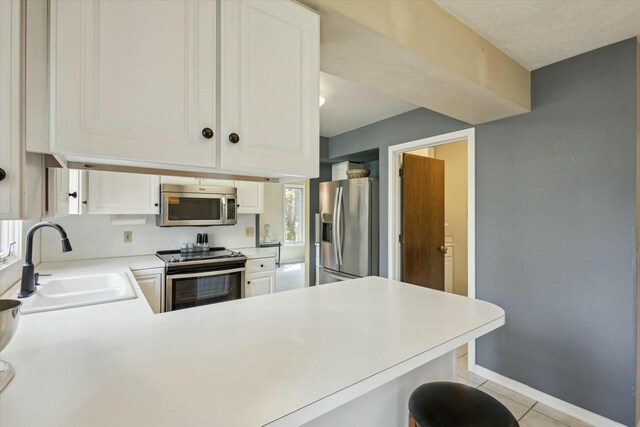 kitchen featuring a sink, light tile patterned floors, light countertops, a peninsula, and stainless steel appliances