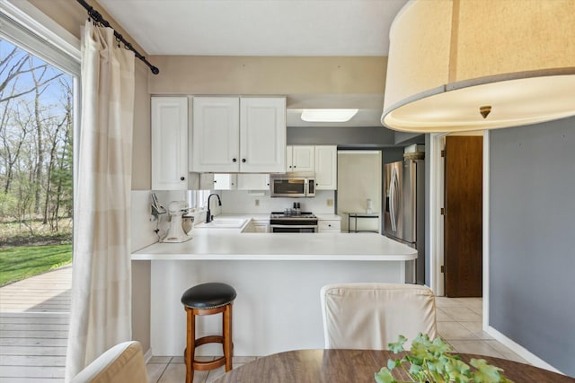 kitchen with a peninsula, light tile patterned flooring, white cabinetry, a sink, and stainless steel appliances