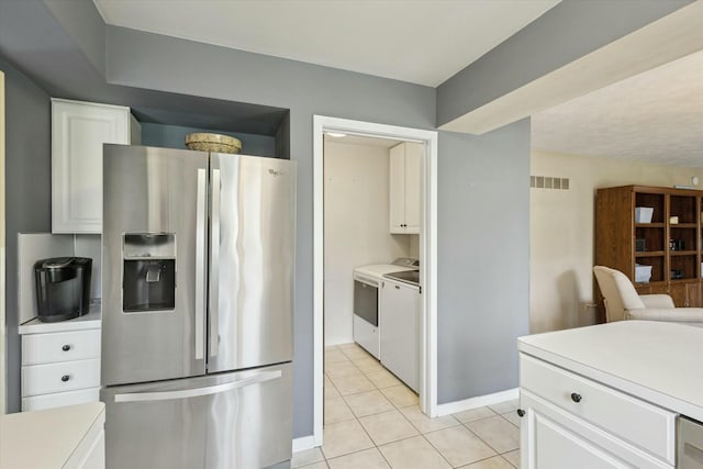 kitchen featuring visible vents, washing machine and dryer, stainless steel fridge, white cabinetry, and light tile patterned floors