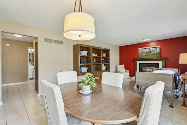 dining area with light tile patterned flooring, baseboards, visible vents, and a glass covered fireplace