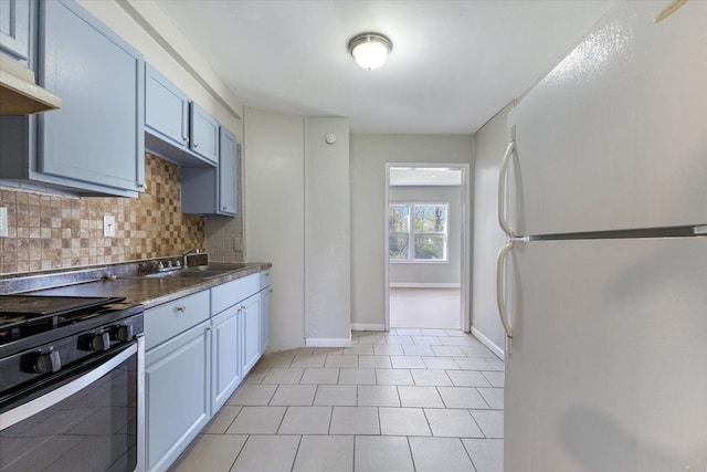 kitchen with backsplash, a sink, light tile patterned floors, stainless steel gas range, and freestanding refrigerator
