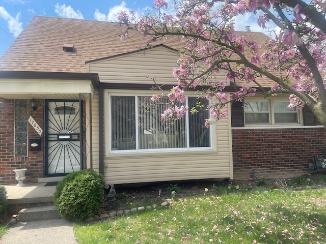 bungalow featuring brick siding, roof with shingles, and a front lawn